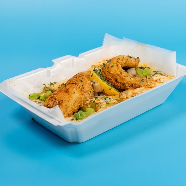 Fried fish fillets with sauce, green peppers, and a lemon wedge in a white takeout container.