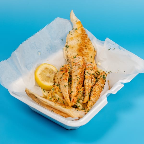 Chicken strips with pasta, a lemon wedge, and garlic bread in a takeout container.