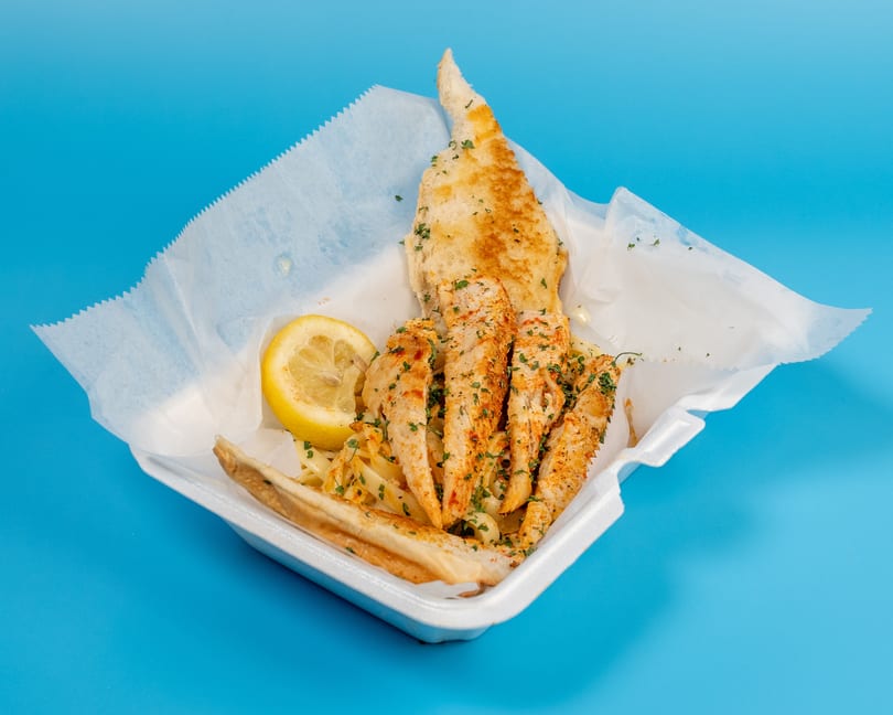 Chicken strips with pasta, a lemon wedge, and garlic bread in a takeout container.
