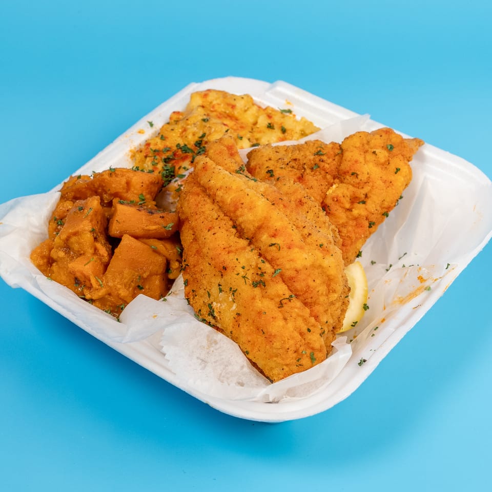 Fried fish fillets, sweet potatoes, and rice in a white takeout container on a blue background.