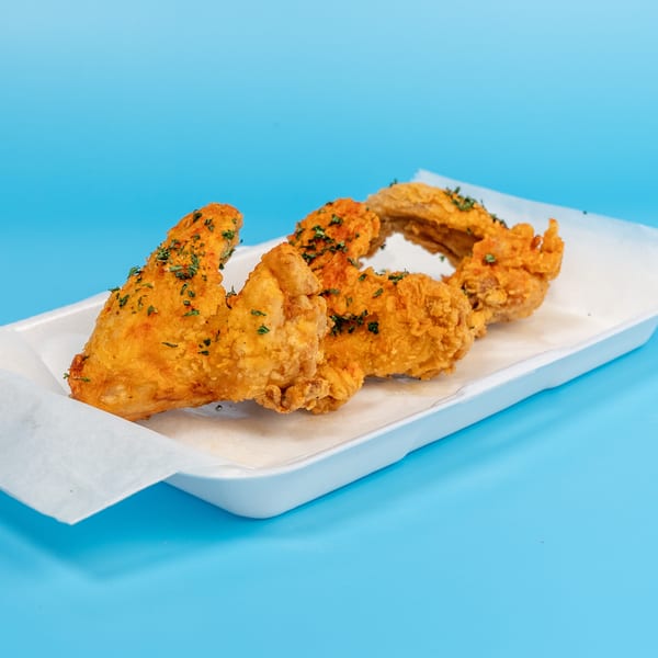 Four golden-brown fried chicken wings with herbs in a white tray on a blue background.