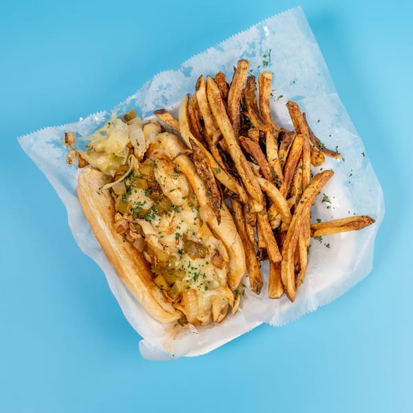 Cheesesteak sandwich with melted cheese, onions, and peppers, served with a side of fries.