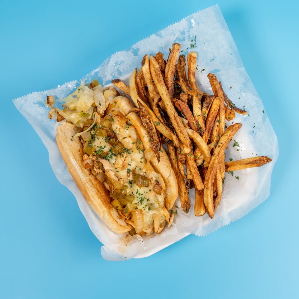 Cheesesteak sandwich with melted cheese, onions, and peppers, served with a side of fries.