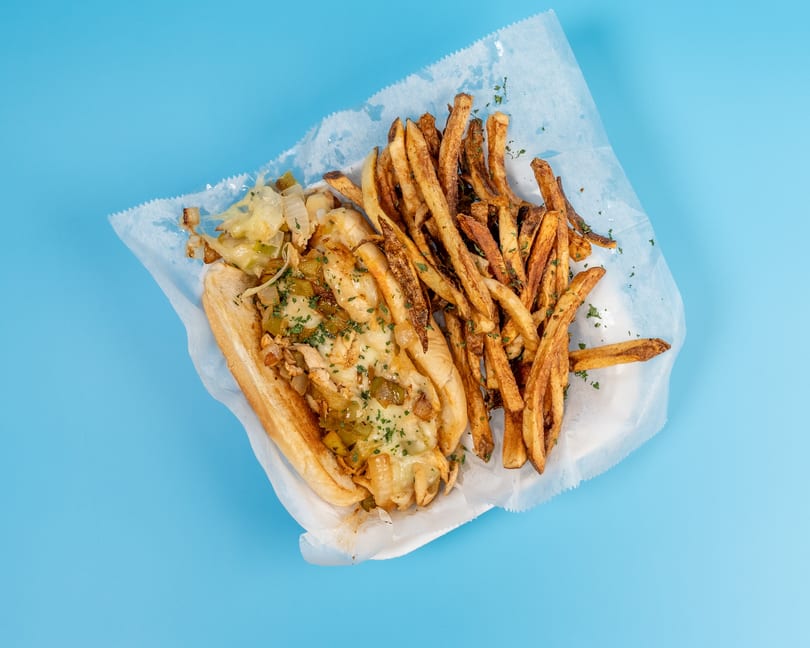 Cheesesteak sandwich with melted cheese, onions, and peppers, served with a side of fries.