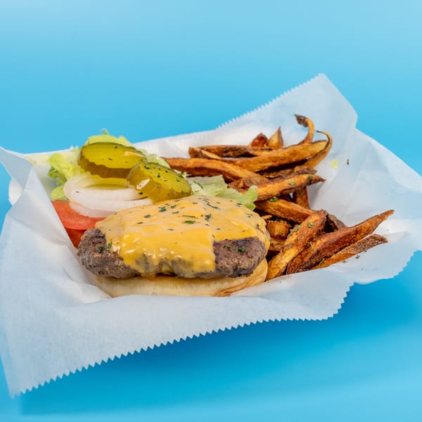 Cheeseburger with lettuce, tomato, onion, pickles, and a side of fries in a paper-lined basket.